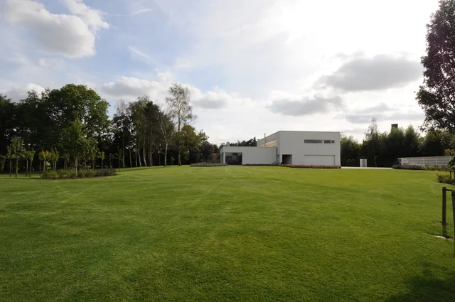 Moderne witte woning op uitgestrekt groen perceel met bomenrijen