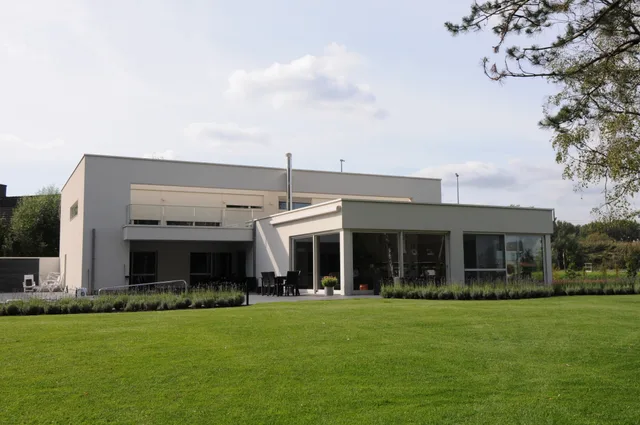 Moderne woning met grijze gevelafwerking en grote glazen oppervlakken, gezien vanaf de tuin
