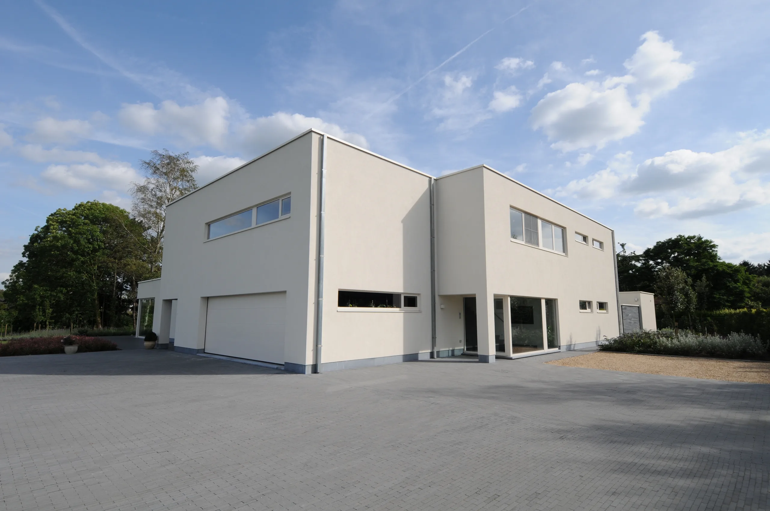 Moderne woning met witte gevelbekleding, grote raampartijen en aangelegraven voorgevel