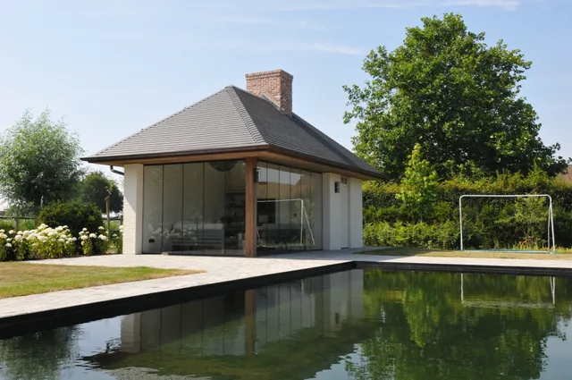 Moderne tuinpaviljoen met grote glaspartijen en zwart dak aan een vijver