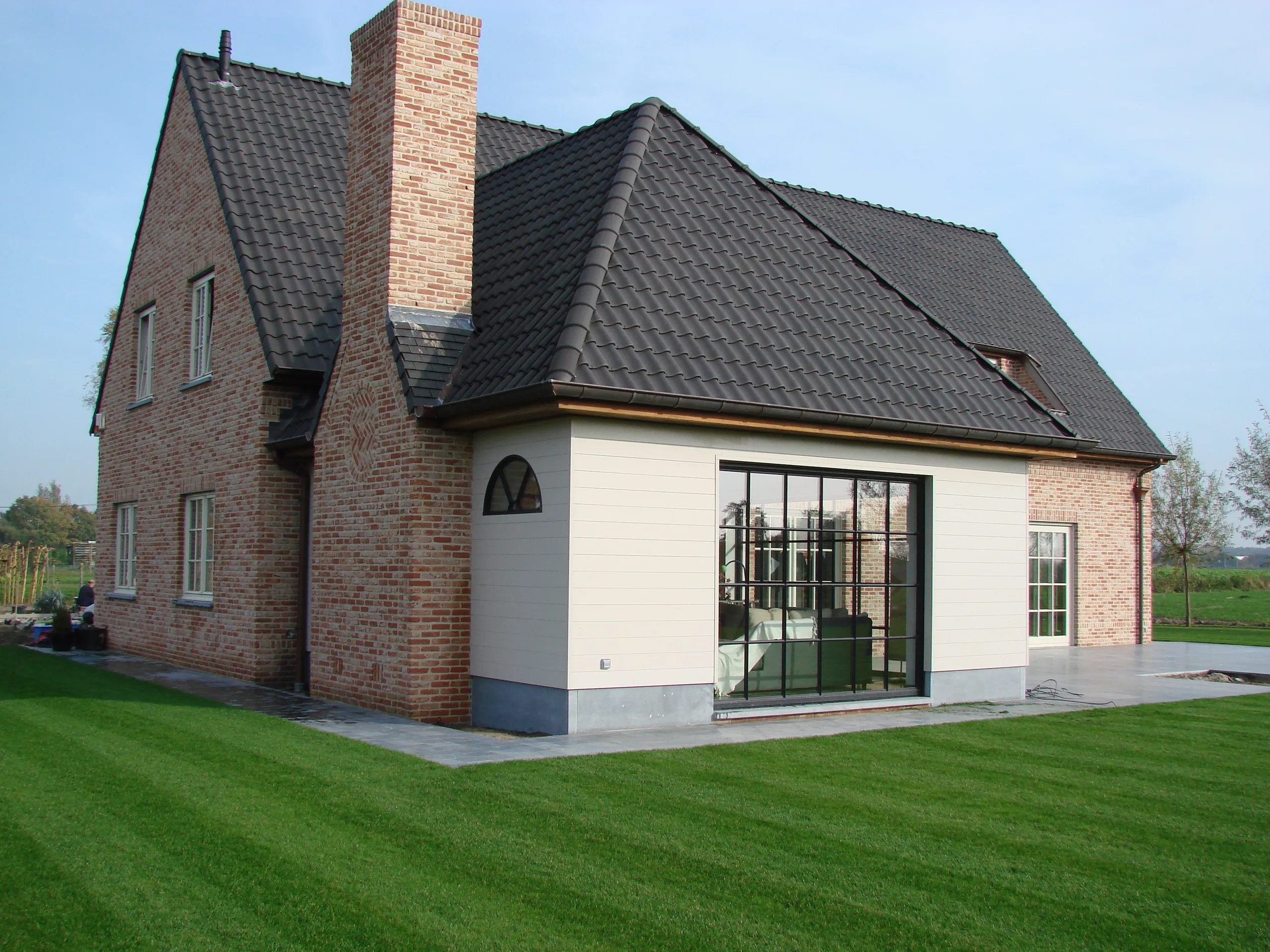 Voorgevel van een nieuwbouwwoning met rode gevelsteen, witte crepi-afwerking en grote raampartijen