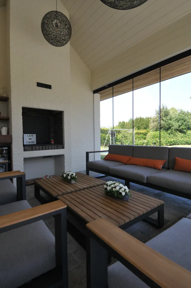 Ruime leefruimte met houten meubels, zwarte zetel en grote glazen wand naar de tuin