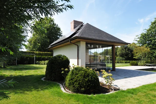 Moderne woning met terrasoverkapping en grote raampartijen aan tuinzijde, omgeven door groenvoorzieningen