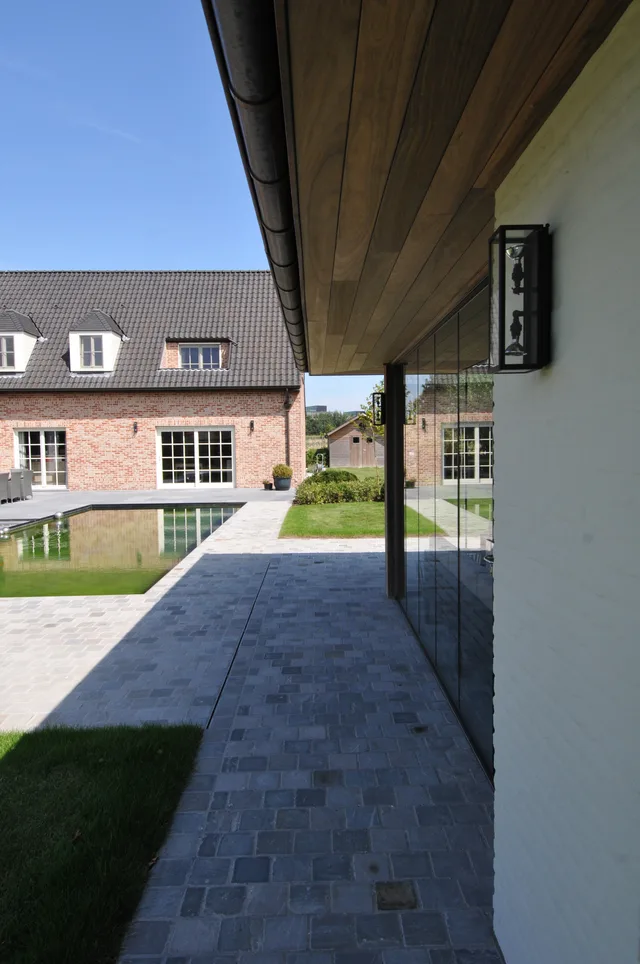 Terrasoverkapping met houten plafond en glazen wand aan tuinzijde van moderne woning met zwembad