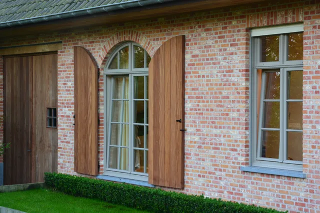 Bakstenen woning met houten luiken rond een gewelfde deur en rechthoekige ramen