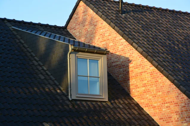 Dakkapel met wit kunststof raamkozijn in rood bakstenen huisgevel bij zonnig weer