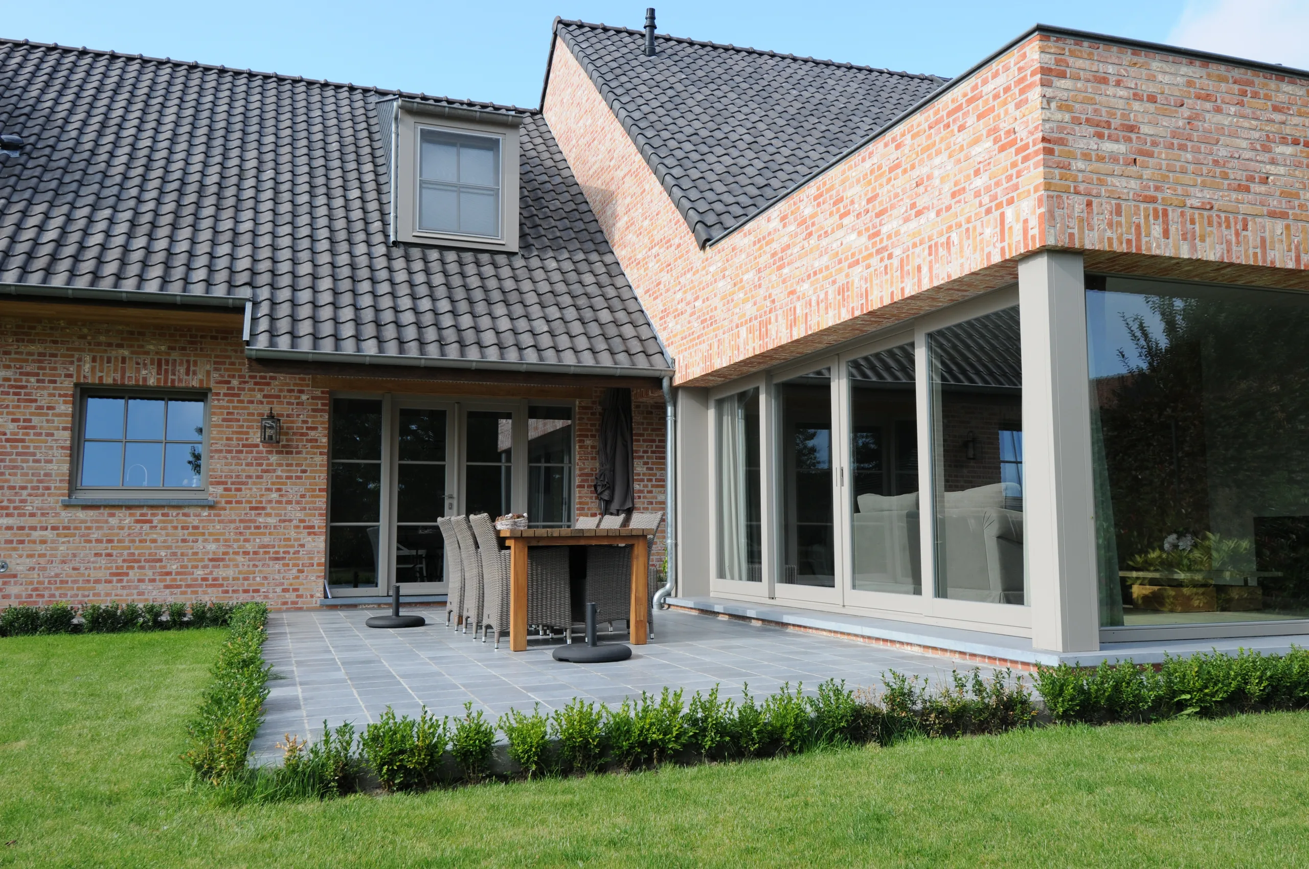 Moderne woning met bakstenen gevel, leisteendak en uitgebreide glazen veranda aan de tuinzijde