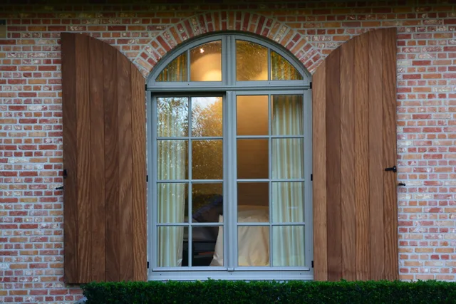Groot raam met grijze sponning en houten luiken op een bakstenen gevel