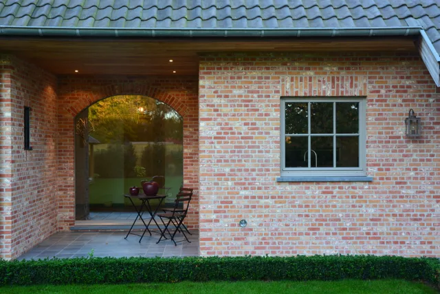 Bakstenen woning met veranda, grote glasdeuren en ramen, tuinmeubels onder het afdak