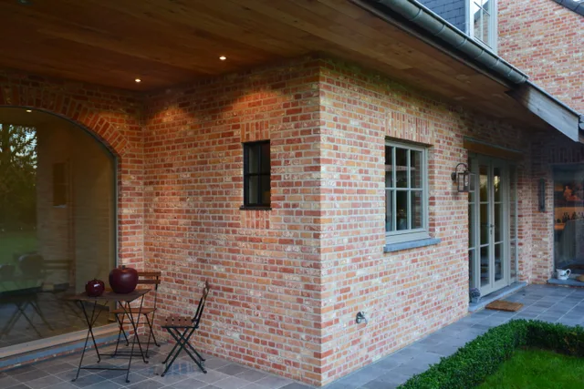 Hoekwoning met bakstenen gevel, overdekt terras en moderne ramen, verlicht door inbouwspotjes