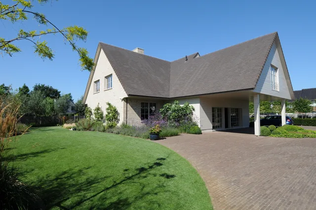 Moderne woning met witte crepi en grijze schilddak, uitkijkend op aangelegde tuin met gazon en terras