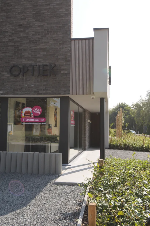 Voorgevel van modern woonhuis met grijze bakstenen muur, verticale metalen luifel en grote glazen ingang
