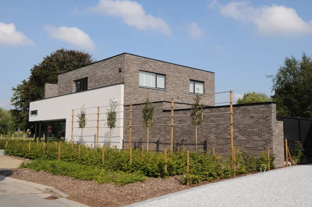 Moderne woning met bakstenen gevel en wit gepleisterde zijde, omgeven door jonge plantjes en houten rankramen