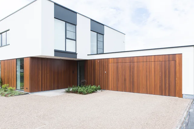 Moderne woning met witte gevel en grote houten garagepoort in bruin hout