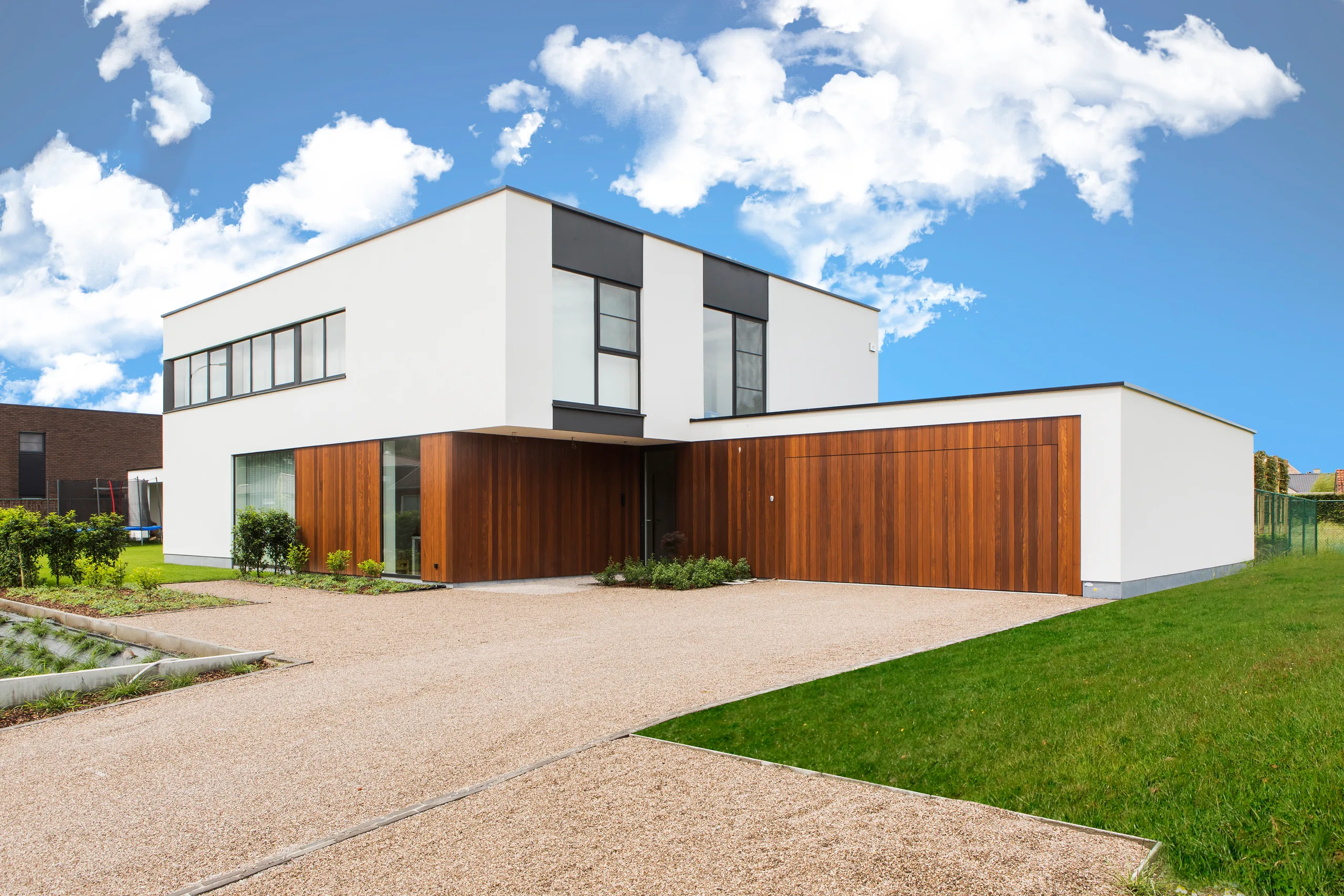 Moderne woning met witte gevel, houten inpandige garage en vlakke daken onder blauwe hemel