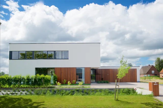 Moderne woning met witte gevel, houten uitbouw en strakke raamlijnen, omgeven door groen en water