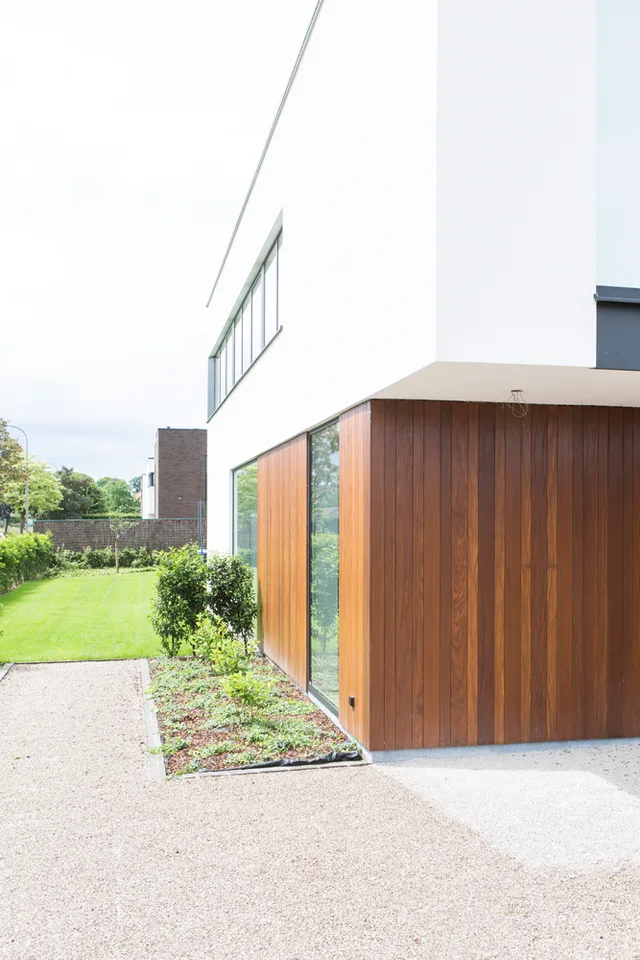 Tuinzijde van een moderne woning met houten bijgebouw en uitzicht op gazon