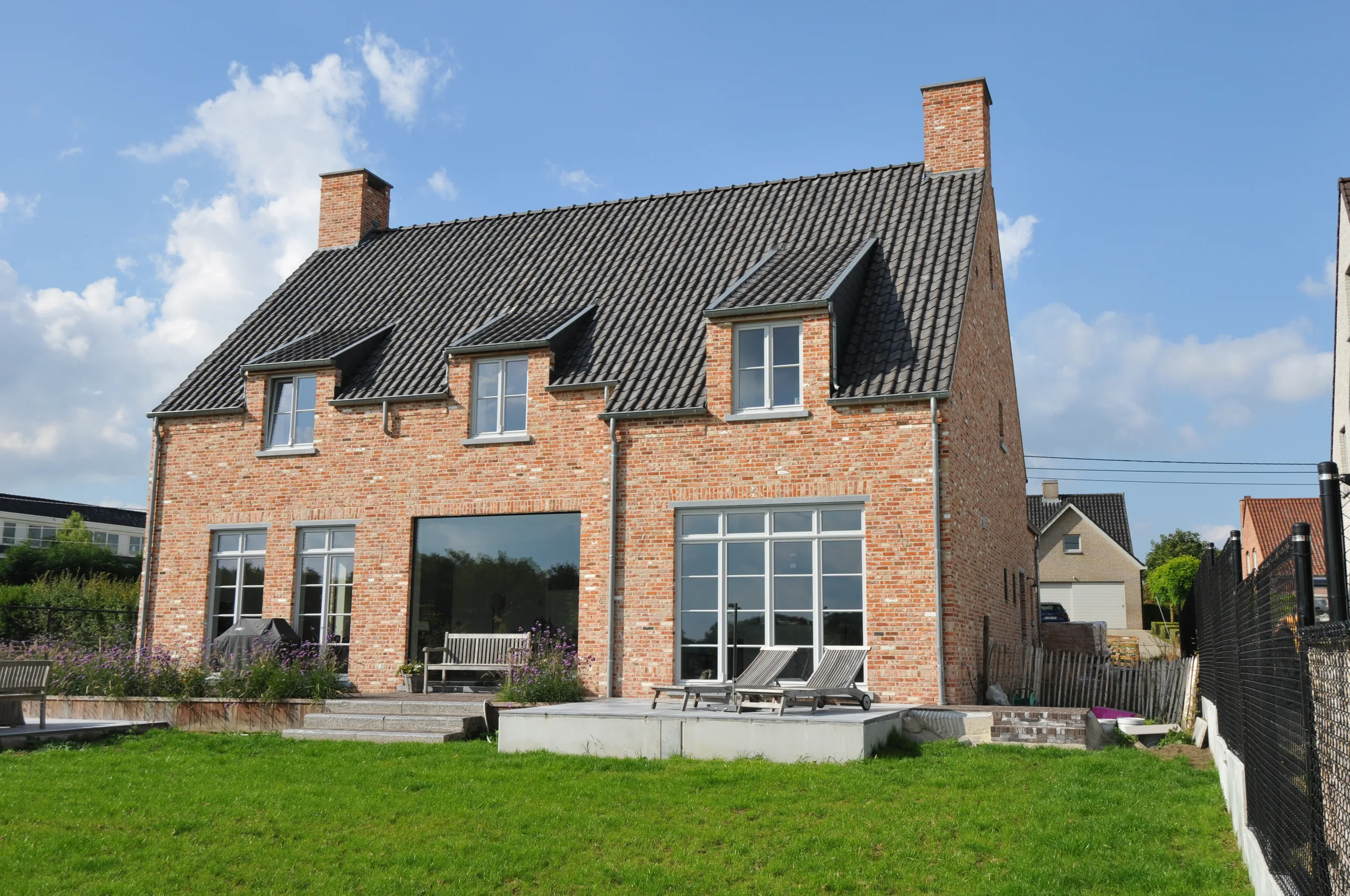Bakstenen woning met schilddak, grote raampartijen en terras, omgeven door groen gazon