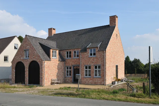 Traditioneel bakstenen huis met uitgebouwde garage onder twee grote boogvormige deuren, in aanbouw