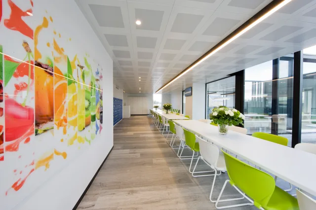 Ruim kantoorgebouw met lange witte zitbank, grote raampartijen en kleurrijke kunstwerk aan de wand