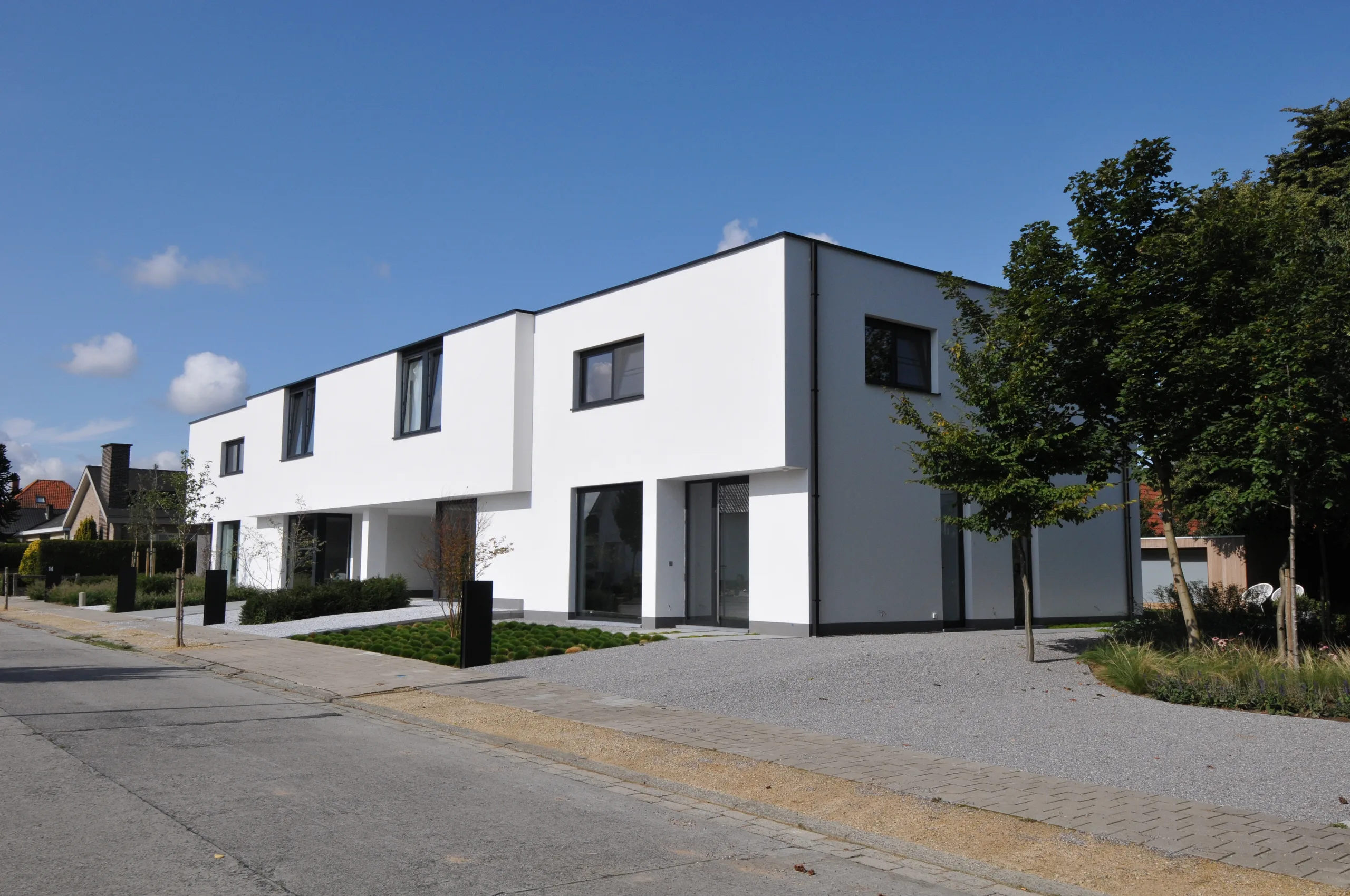 Moderne witte villa met grote raampartijen en minimalistische voorgevelarchitectuur