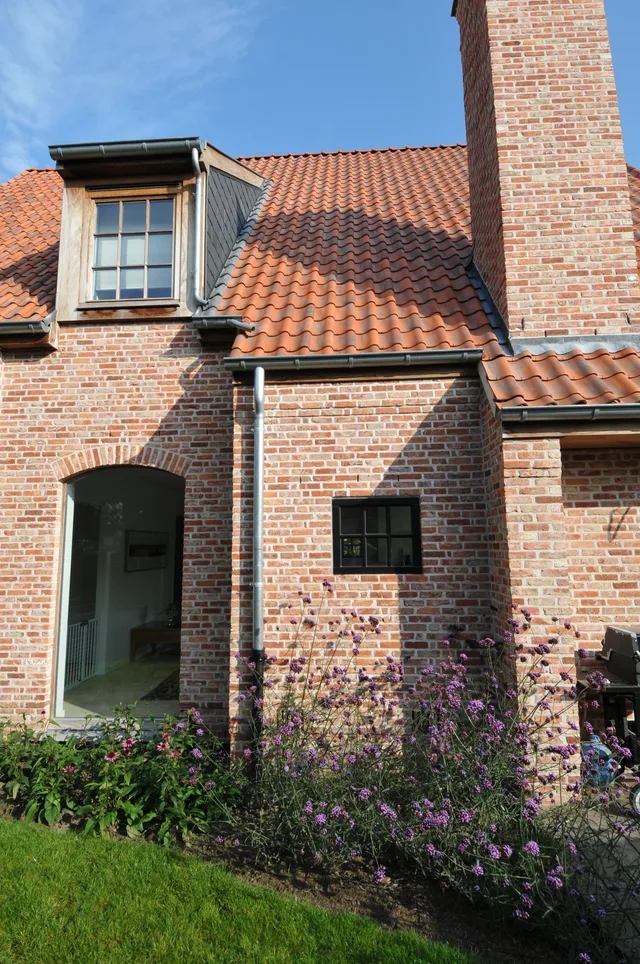 Bakstenen voorgevel met dakkapel, oranje dakpannen en voortuin met paarse bloemen