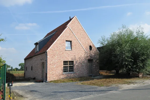 Bakstenen woning met zadeldak en dakkapel aan een landelijke weg