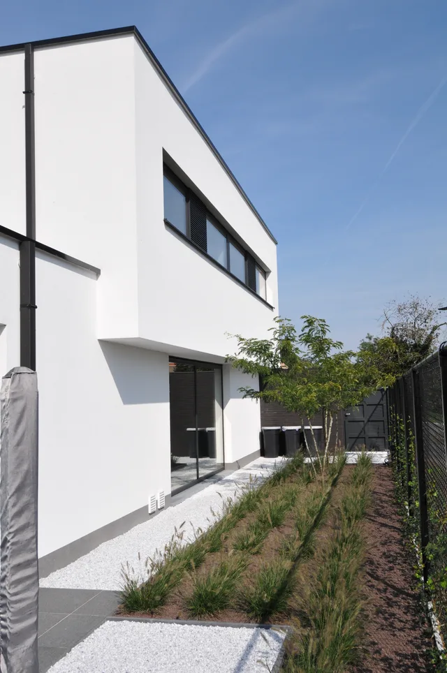 Moderne woning met witte gevel, zwarte raamlijsten en aangelegde voortuin met grindverharding