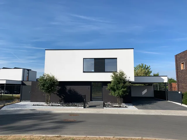 Moderne woning met witte bovenbouw en donkere onderetage, grote raampartijen en carport