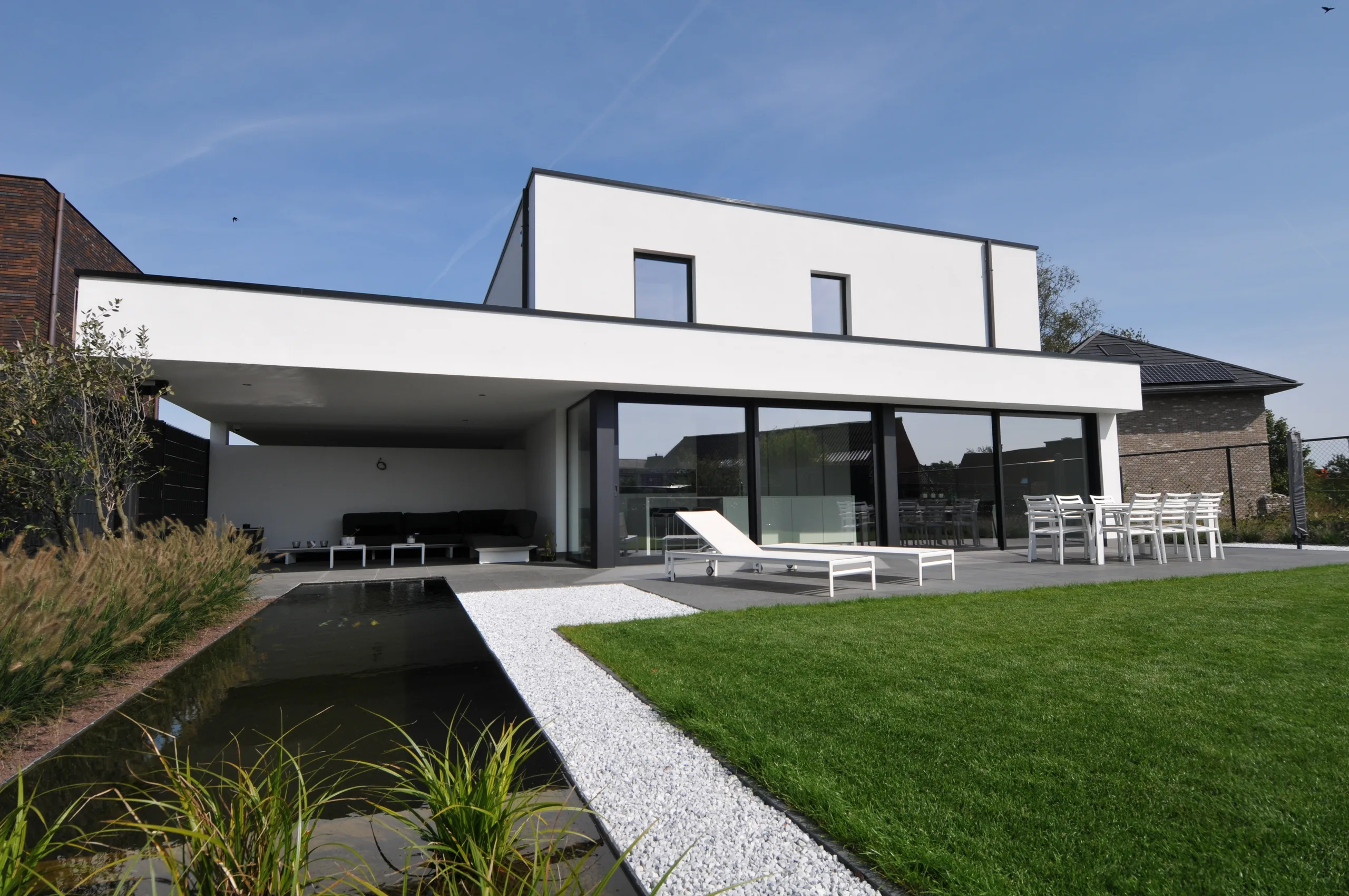Moderne woning met witte gevel, grote glaspartijen en terrasoverkapping aan de tuinzijde