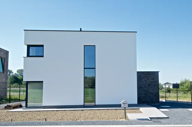 Minimalistische voorgevel van een woning met witte crepi, grote raampartijen en donkere accenten