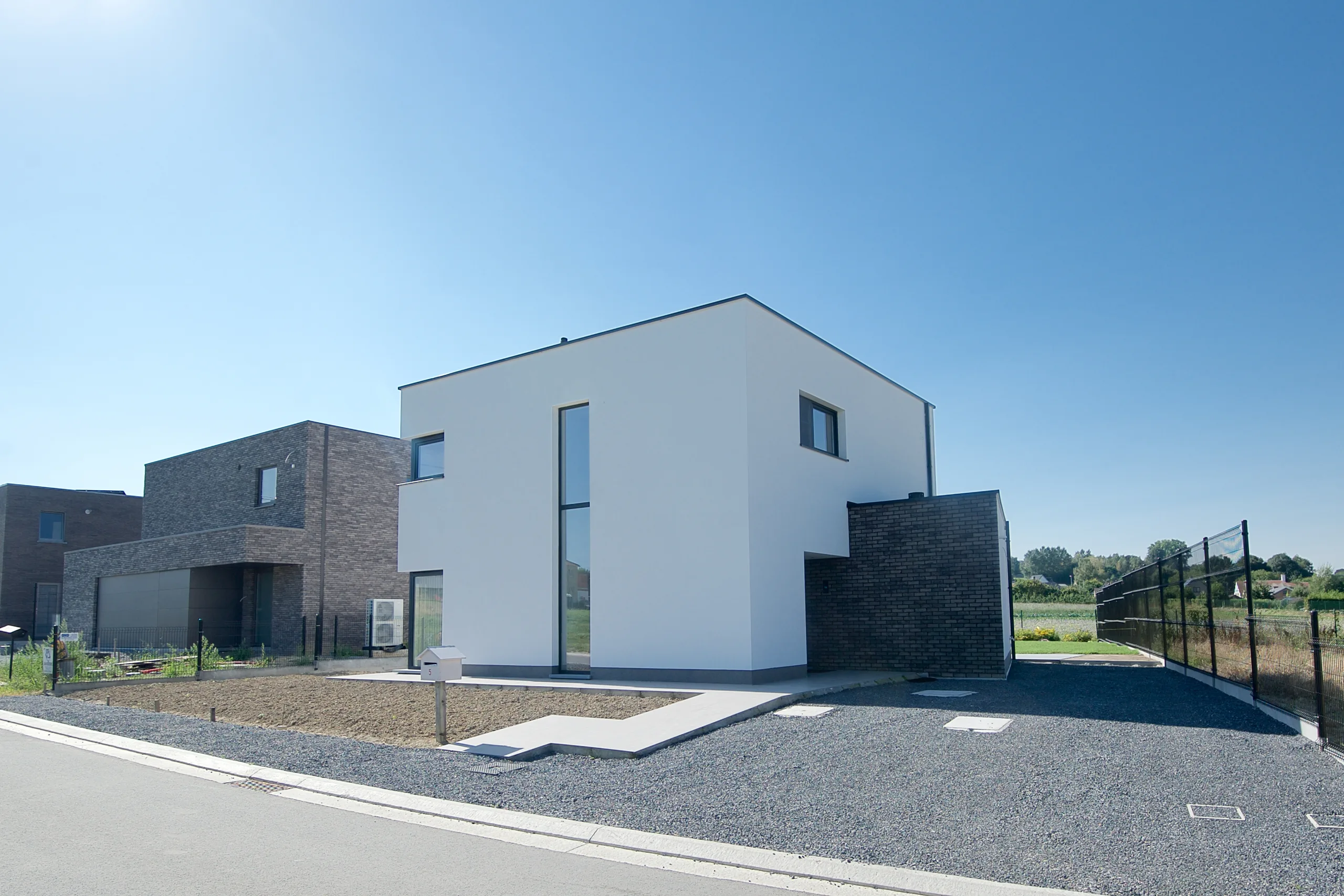 Nieuwbouwwoning met witte gevelbekleding en rode gevelsteen, gezien vanaf de straat