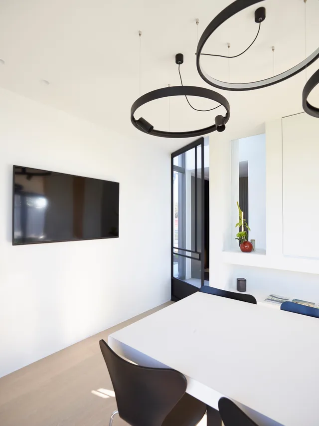 Minimalistisch kantoor met witte wanden, zwarte ronde designlampen en grote raampartijen