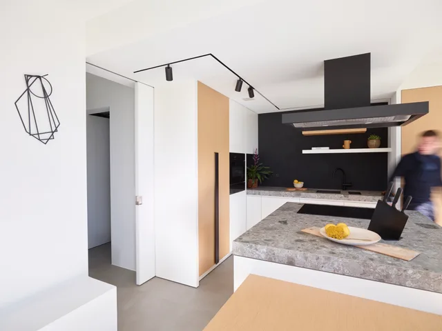 Open keuken met groot eiland in beton-ciré, zwarte achterwand en houten accenten