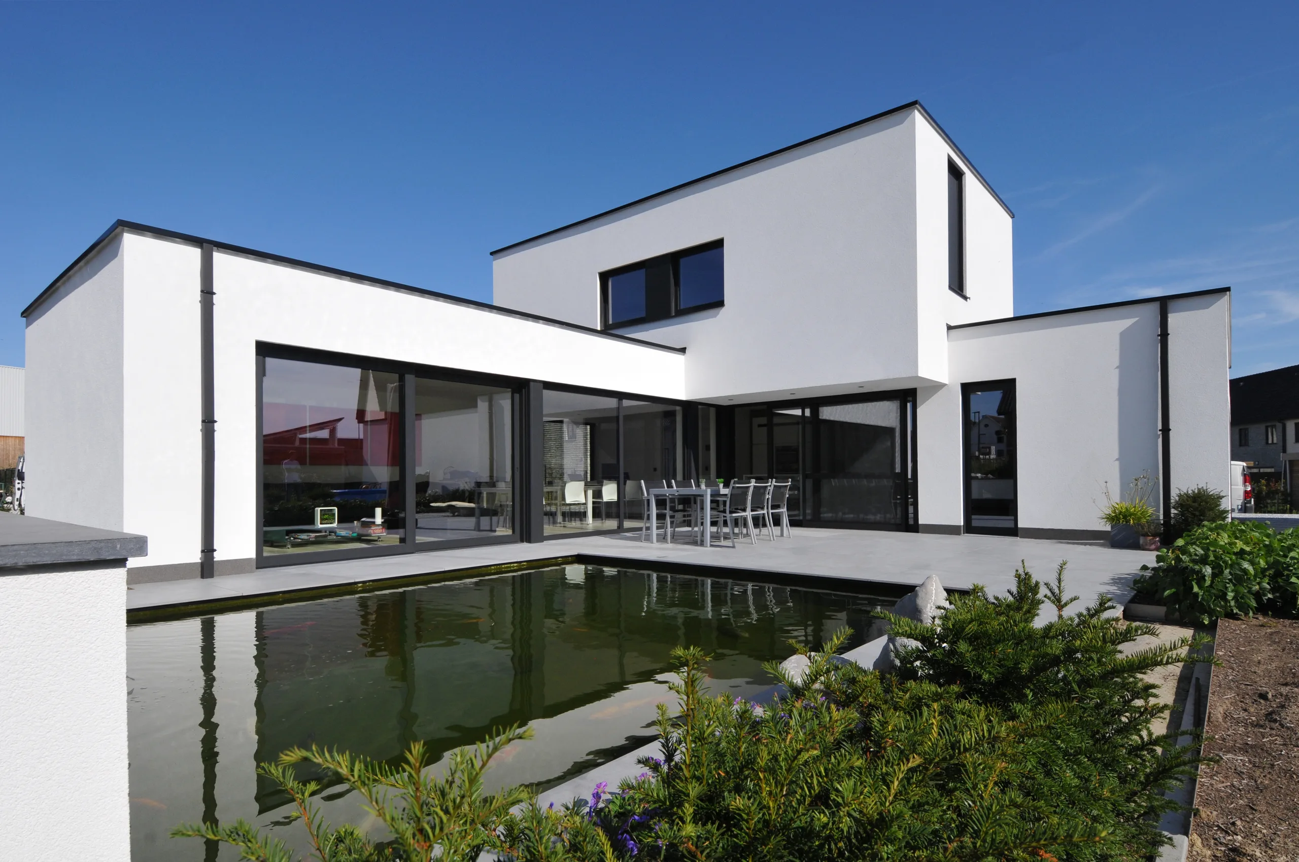 Moderne witte woning met platte daken en grote raampartijen, omgeven door water en groene beplanting