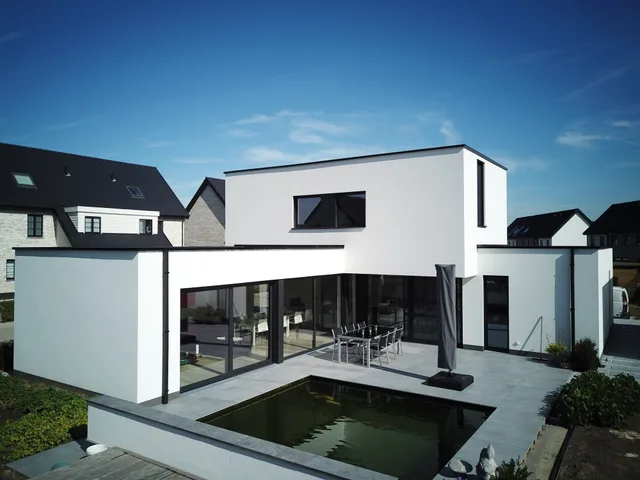 Moderne witte woning met vlakke daken, grote glazen schuifdeuren en aangelegde vijver op de voortuin