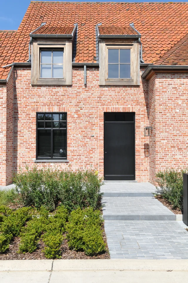 Voorgevel van een woning met bakstenen muur, dakkapel met houten kozijnen en zwarte deur