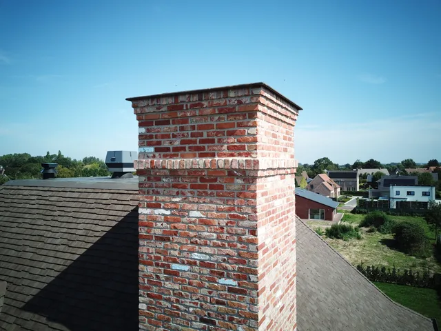 Bakstenen schoorsteen op een hellend dak met uitzicht over de buurt