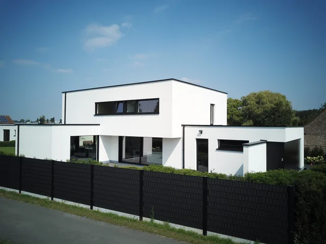 Moderne woning met witte gevel, zwarte raampartijen en plat dak achter zwarte erfafscheiding