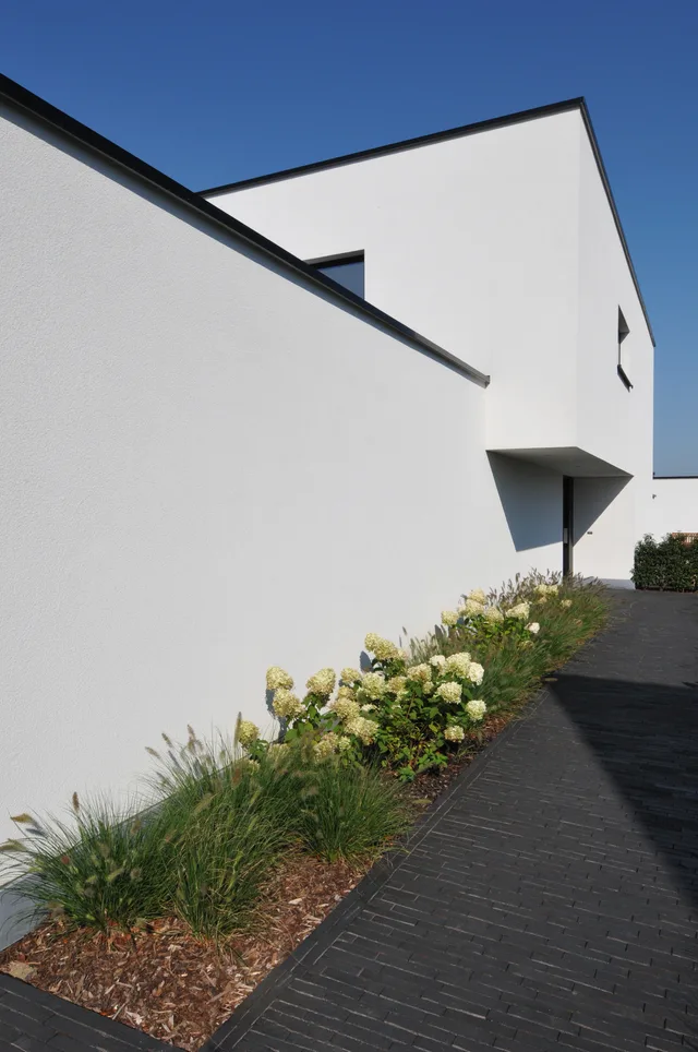 Witte voorgevel van moderne woning met tuinbeplanting langs de ingang