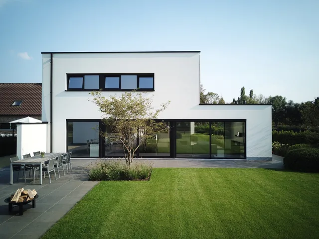 Moderne woning met witte gevel en grote glaspartijen, uitzicht op terras en tuin