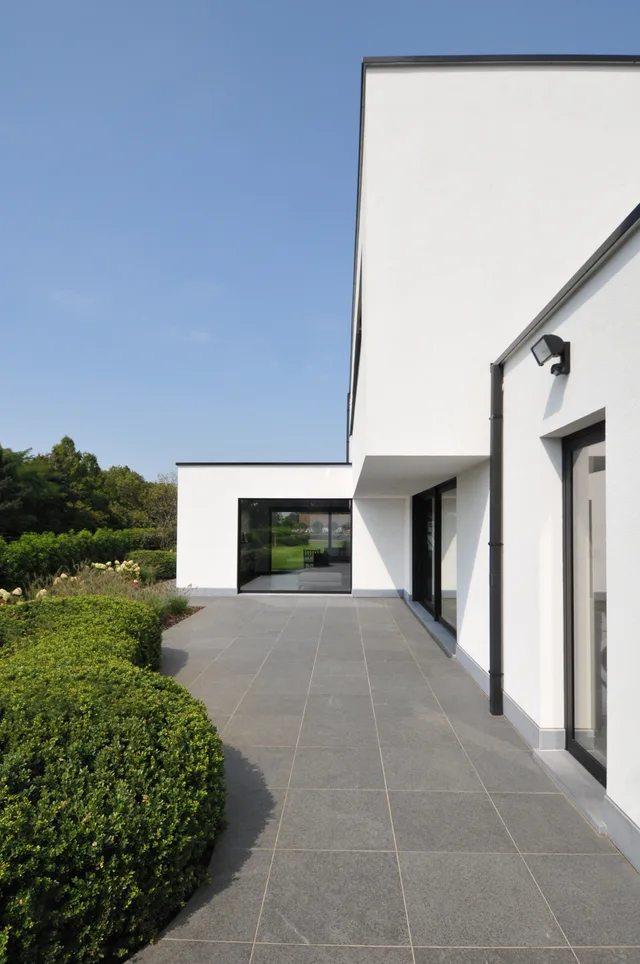 Moderne woning met witte gevel en grote glaspartijen aan de tuinzijde, met terras van grijze tegels
