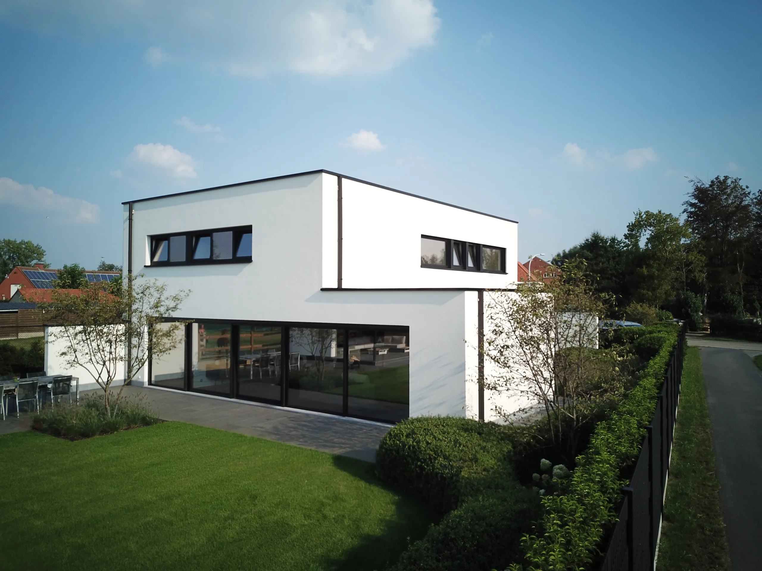Moderne woning met witte gevel, grote zwarte raampartijen en groen grasveld aan de voorkant