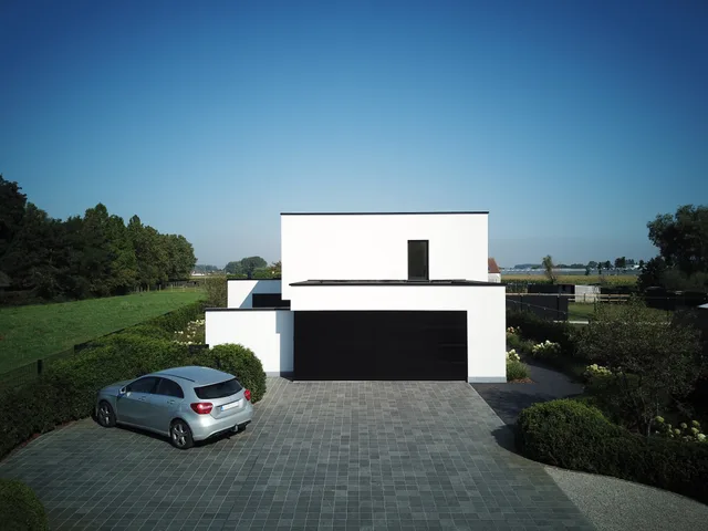 Moderne woning met witte gevelbekleding en zwarte accenten in landelijk omgeving