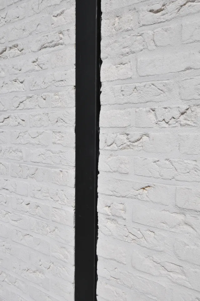 Detailopname van een witte bakstenen muur met een zwarte stalen voeg in het midden