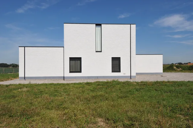 Voorgevel van een modern witte woning met stalen raamlijsten en grijze samenhangende sokkel op een landelijk perceel