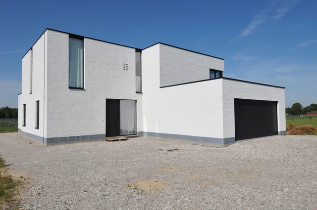 Moderne woning met witte gevelsteen en grote raampartijen, gezien vanaf de voortuin
