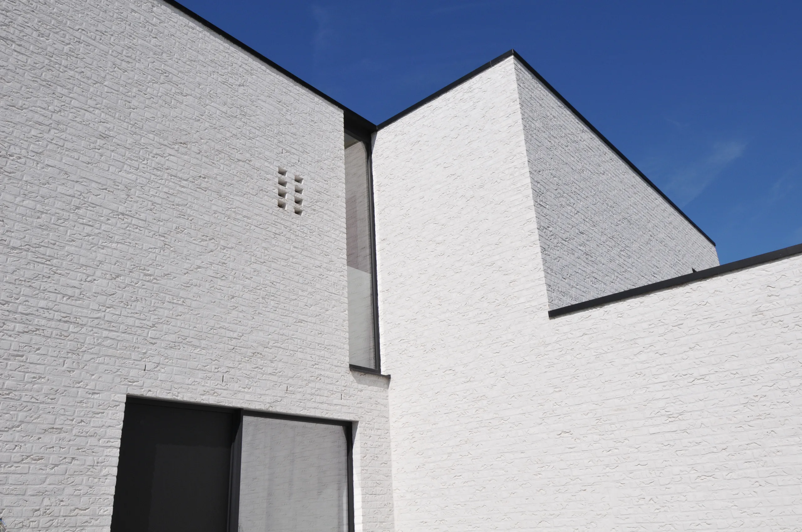 Voorgevel van een moderne woning met witte baksteenafwerking en zwarte raamkozijnen