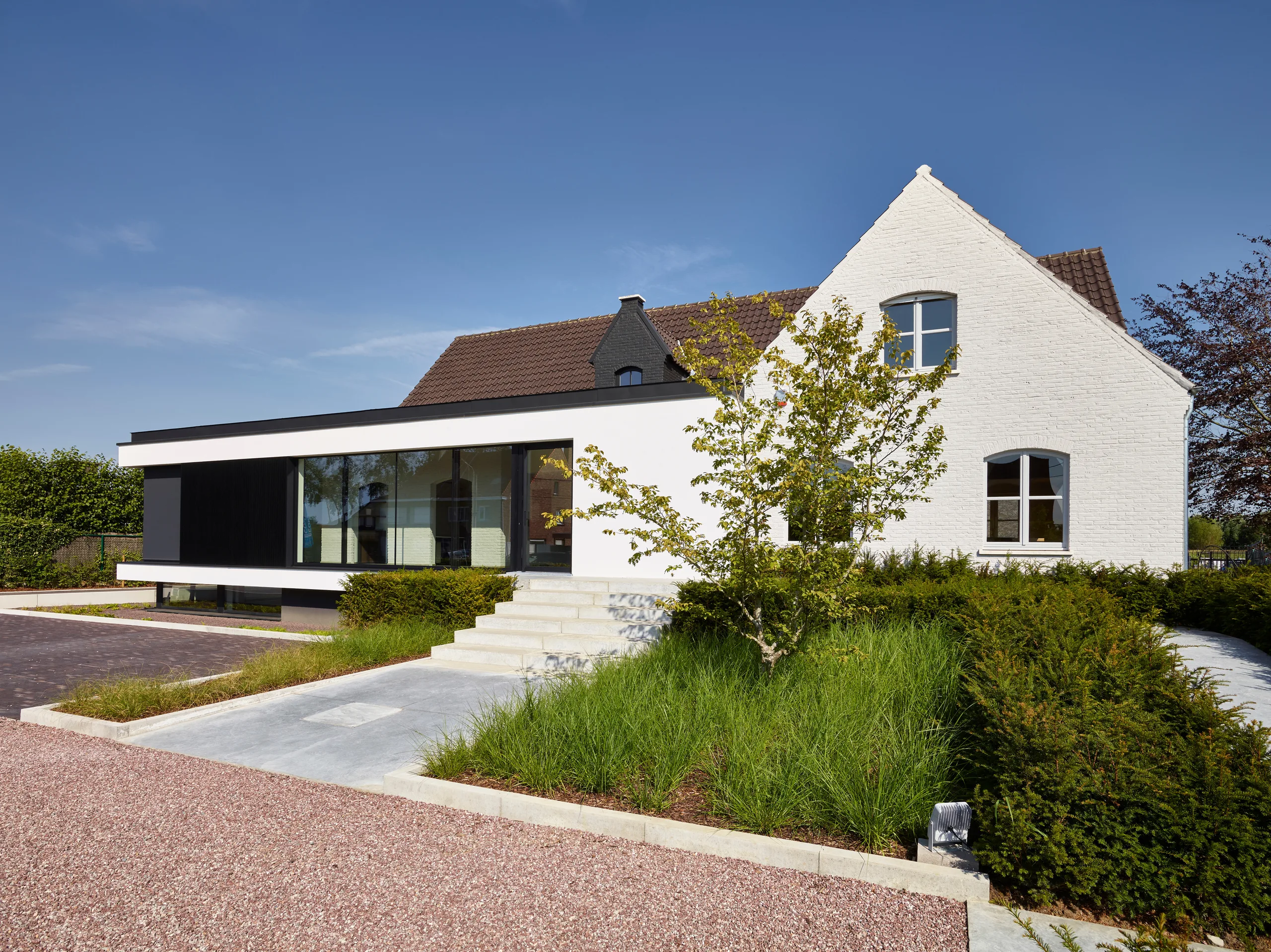 Woning met witte gevel en moderne aanbouw met grote glazen pui, voorgevel