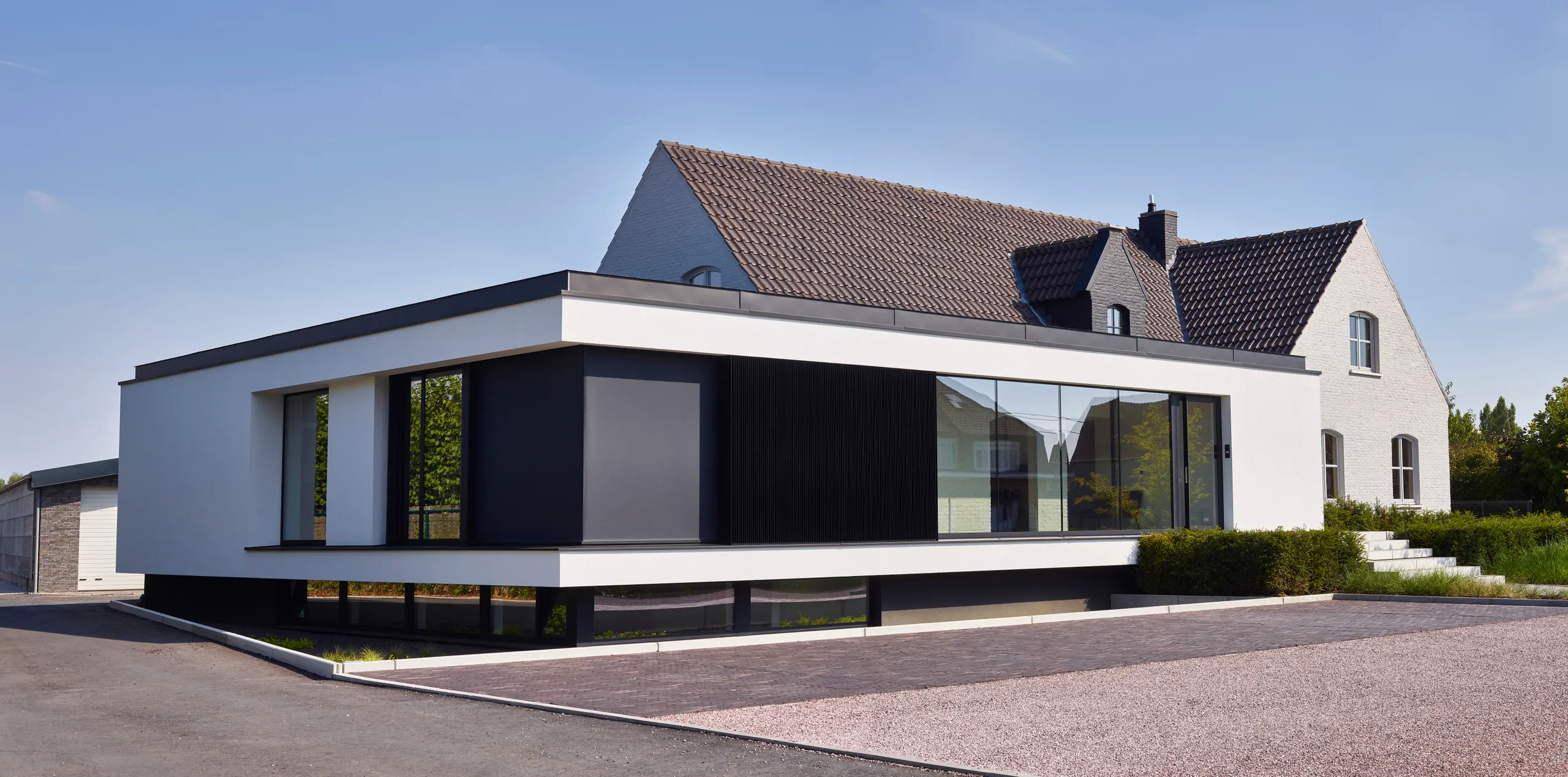 Moderne witte uitbouw met grote raampartijen tegen traditioneel huis met pannendak